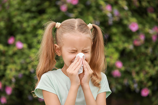 A young girl holding a tissue blows her nose